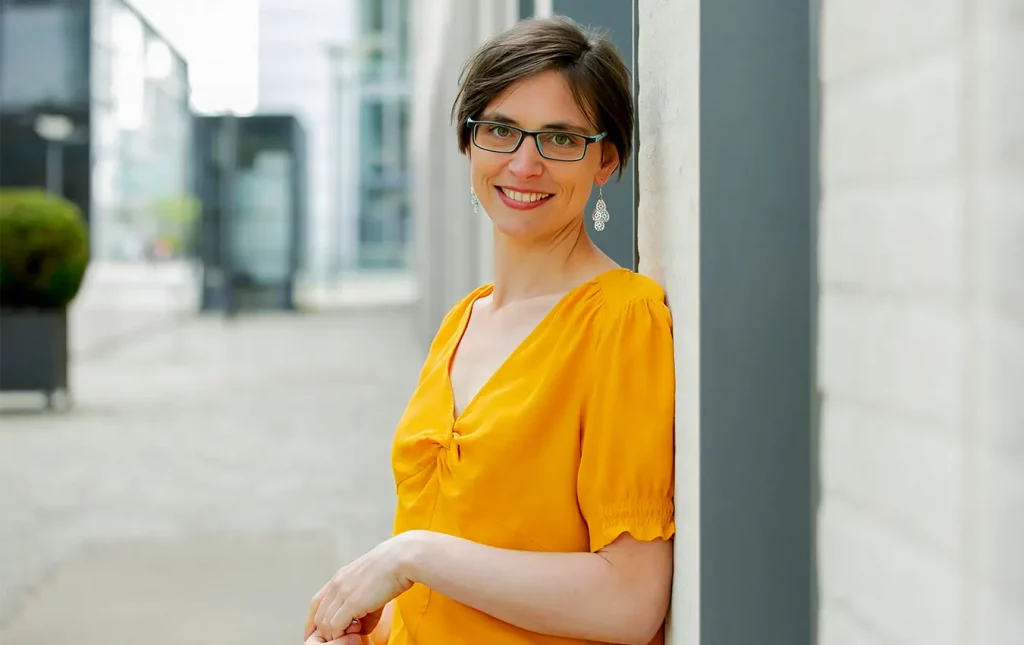 Sarah Gierhan vor einer Fassade, sie trägt ein gelbes Oberteil